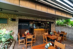 An outdoor cafe area with wooden tables and chairs, a stone wall, and a sign for 'CINQ & CASTOR CAFE RESTAURANT'. - Candelaria Aparta Hotel Boutique  (Medellín)