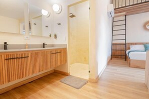 A modern bathroom with a wooden vanity, a glass shower enclosure, and a bed with a wooden headboard. - Candelaria Aparta Hotel Boutique  (Medellín)