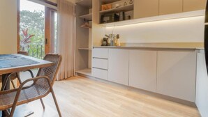 Een moderne keuken met witte kastjes, een eethoek met een houten tafel en rieten stoelen, en uitzicht op groen.