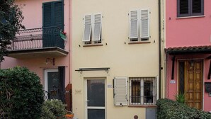Ein Gebäude mit einer Tür, Fenstern mit Fensterläden, einem Balkon und einem kleinen Garten.