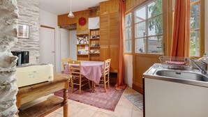 Une cuisine avec une table en bois, des chaises, un évier et un mur en pierre.