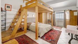 Une pièce avec un lit superposé en bois, une petite table, une chaise, un radiateur et une fenêtre.