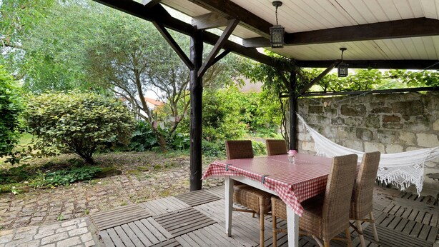 Une terrasse extérieure avec une table et des chaises, un hamac et un mur en pierre.