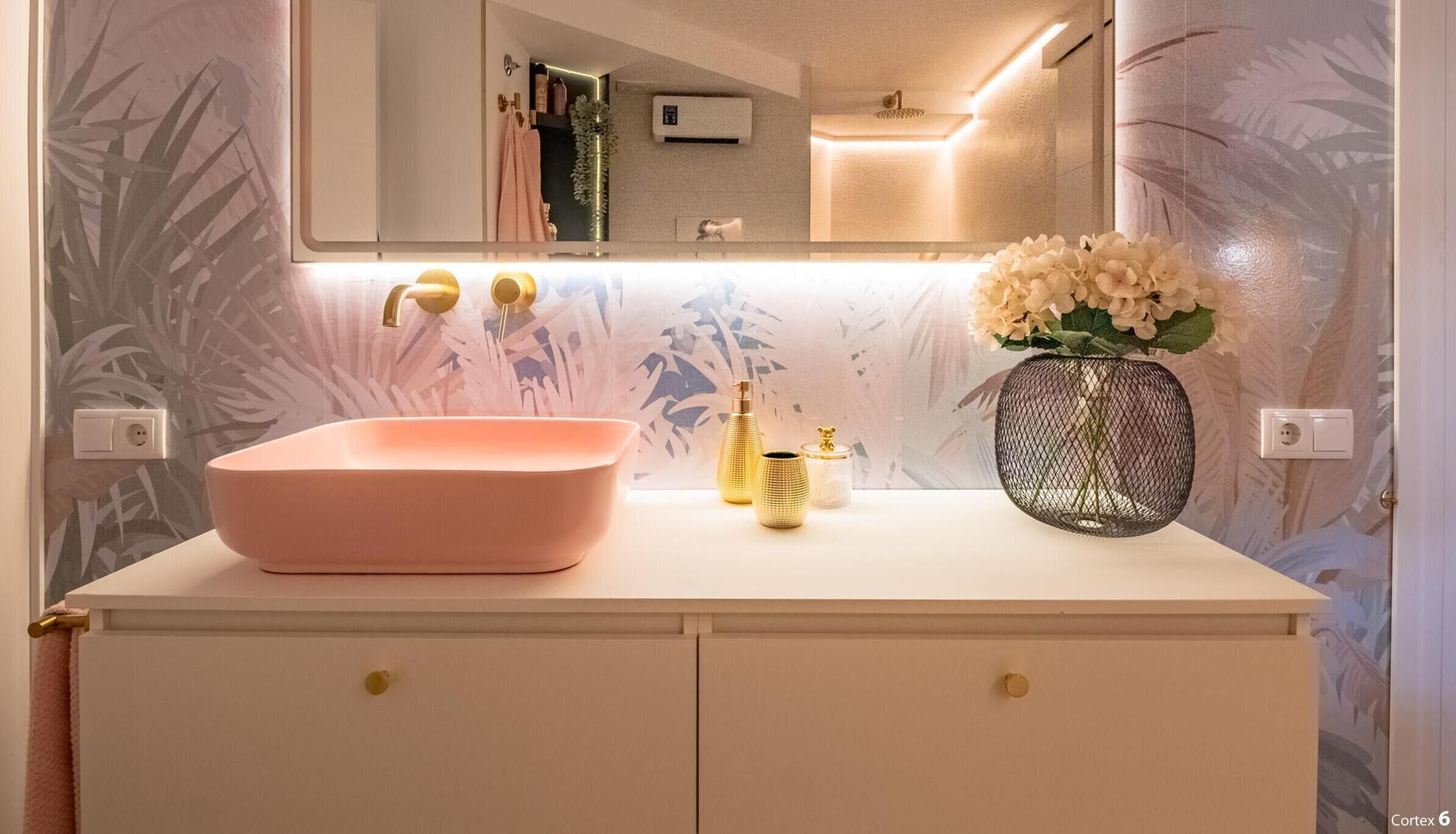 Un baño con un lavamanos rosa, detalles dorados y un florero con flores.