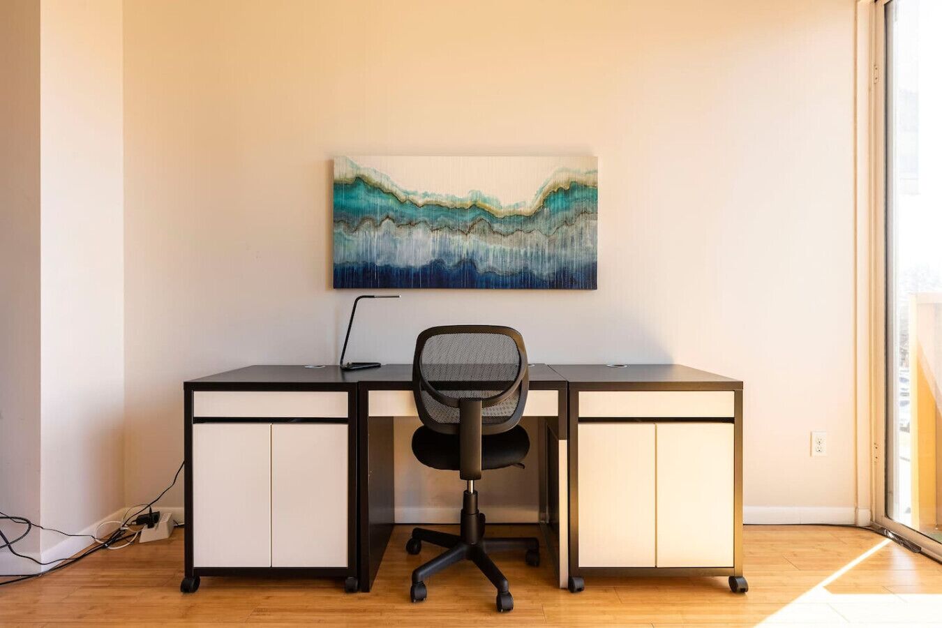 A modern office desk with a laptop, a chair, and a painting on the wall.