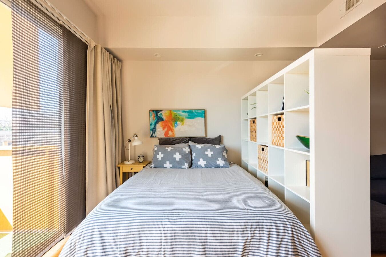 A bedroom with a bed, a nightstand, a painting, and built-in storage.