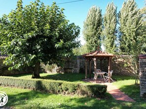 Un jardín con un pabellón, un muro de piedra y un árbol grande.