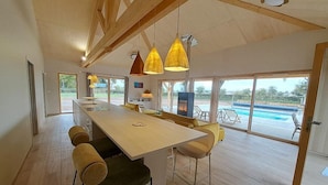 A spacious kitchen with a long island, modern pendant lights, and a view of a pool through large windows. - Cozy Lodge in Vivans with Pool and Spa, Pets Allowed (Vivans)