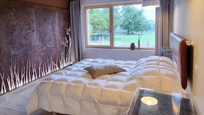 A bedroom with a large bed, a window with a view of greenery, and a modern pendant light. - Cozy Lodge in Vivans with Pool and Spa, Pets Allowed (Vivans)