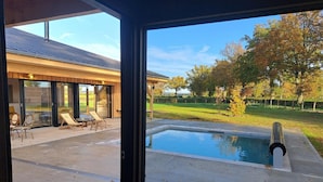 A modern house with a glass door leading to a patio with a pool, outdoor furniture, and a view of a grassy area with trees. - Cozy Lodge in Vivans with Pool and Spa, Pets Allowed (Vivans)