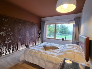 A bedroom with a large bed, a window with a view of greenery, and a wall with a nature-themed design. - Cozy Lodge in Vivans with Pool and Spa, Pets Allowed (Vivans)