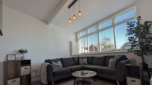 A modern living room with a sectional sofa, a round coffee table, and a large window with blinds. - House in Martham (GREAT YARMOUTH)