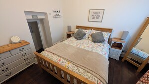 A bedroom with a wooden bed, floral bedding, a bedside table with a lamp, a mirror, and a dresser with drawers. - House in Martham (GREAT YARMOUTH)