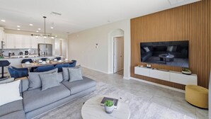 Uma sala de estar moderna com um sofá cinzento, uma mesa de centro e uma TV fixada numa parede de madeira.