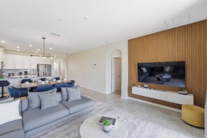 A modern living room with a grey sofa, a coffee table, and a TV mounted on a wooden wall. - 3BR Retreat at ChampionsGate near Disney (Kissimmee)