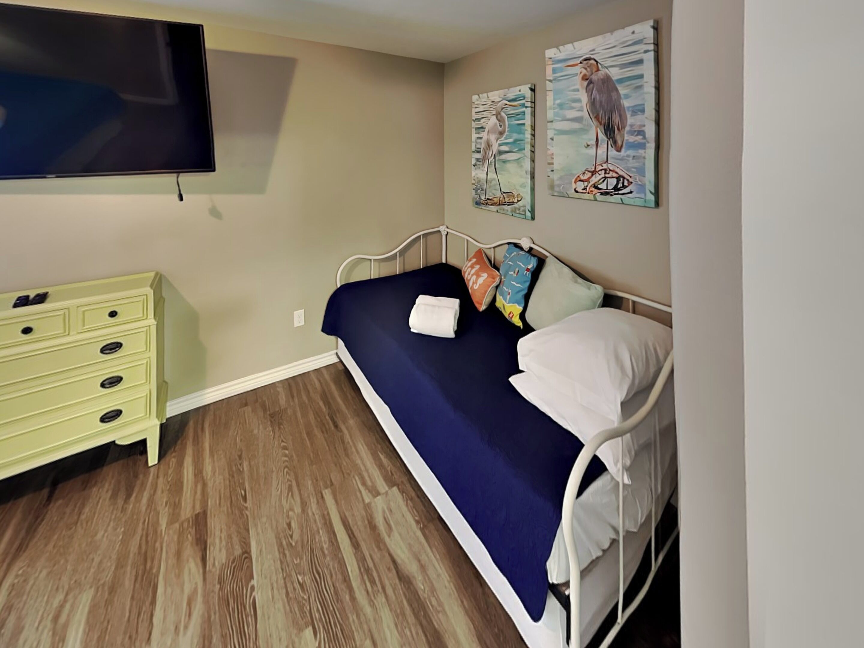 Une chambre à coucher comprenant un lit, une commode, un téléviseur à écran plat et deux tableaux accrochés au mur.