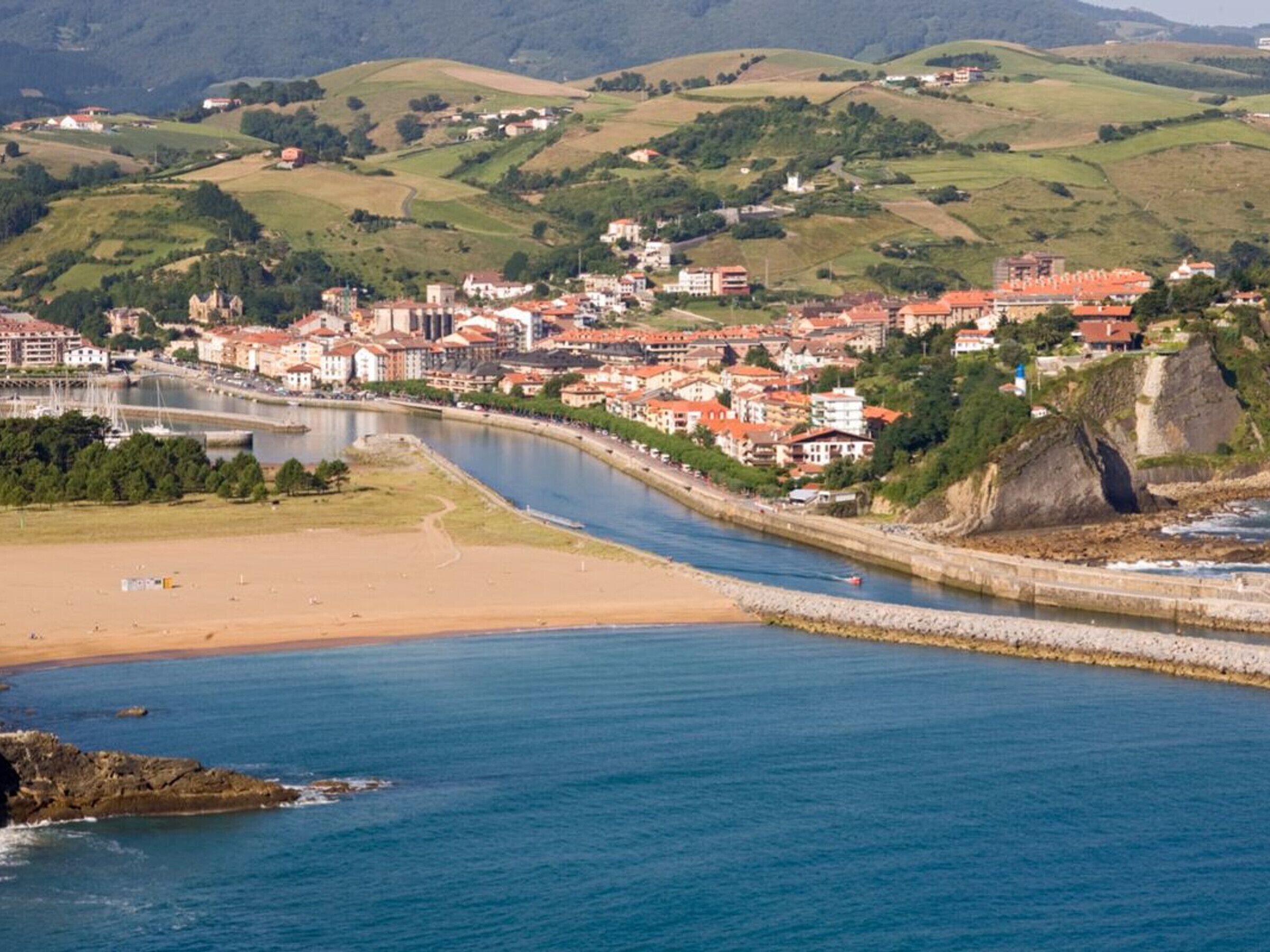 Eine Küstenstadt mit Fluss, Sandstrand und Häusern mit roten Dächern.