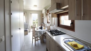 A compact kitchen with wooden cabinets, a gas stove, and a dining area with a table and chairs. - Bungalow For 4, Terrace - Zumaia, Spain (Zumaya)