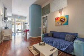 Een woonkamer met een blauwe bank, een witte salontafel en een trap naar een balkon.