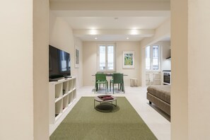 Ein modernes Wohnzimmer mit Flachbildfernseher, einer Couch, einem Essbereich mit Stühlen und einer Küche im Hintergrund.