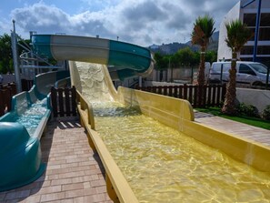 Un toboggan aquatique avec un canal d’eau transparent, un chemin en briques et une clôture en bois.