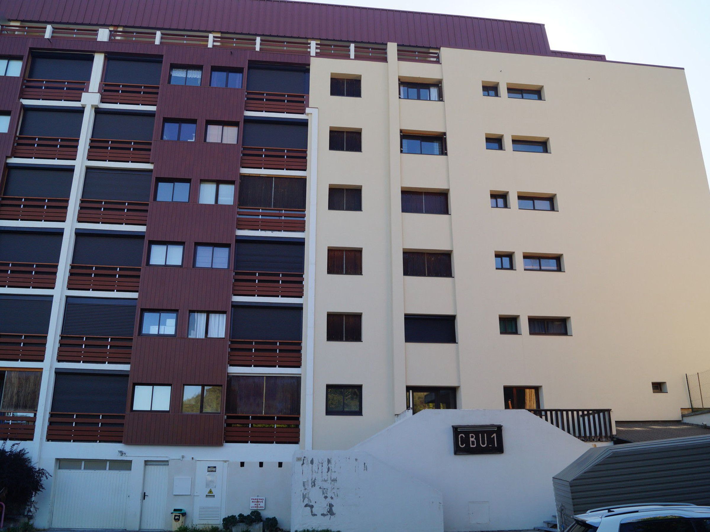 Un immeuble à plusieurs étages, dont la façade présente un mélange de styles de fenêtres et une enseigne indiquant « CBU1 ».