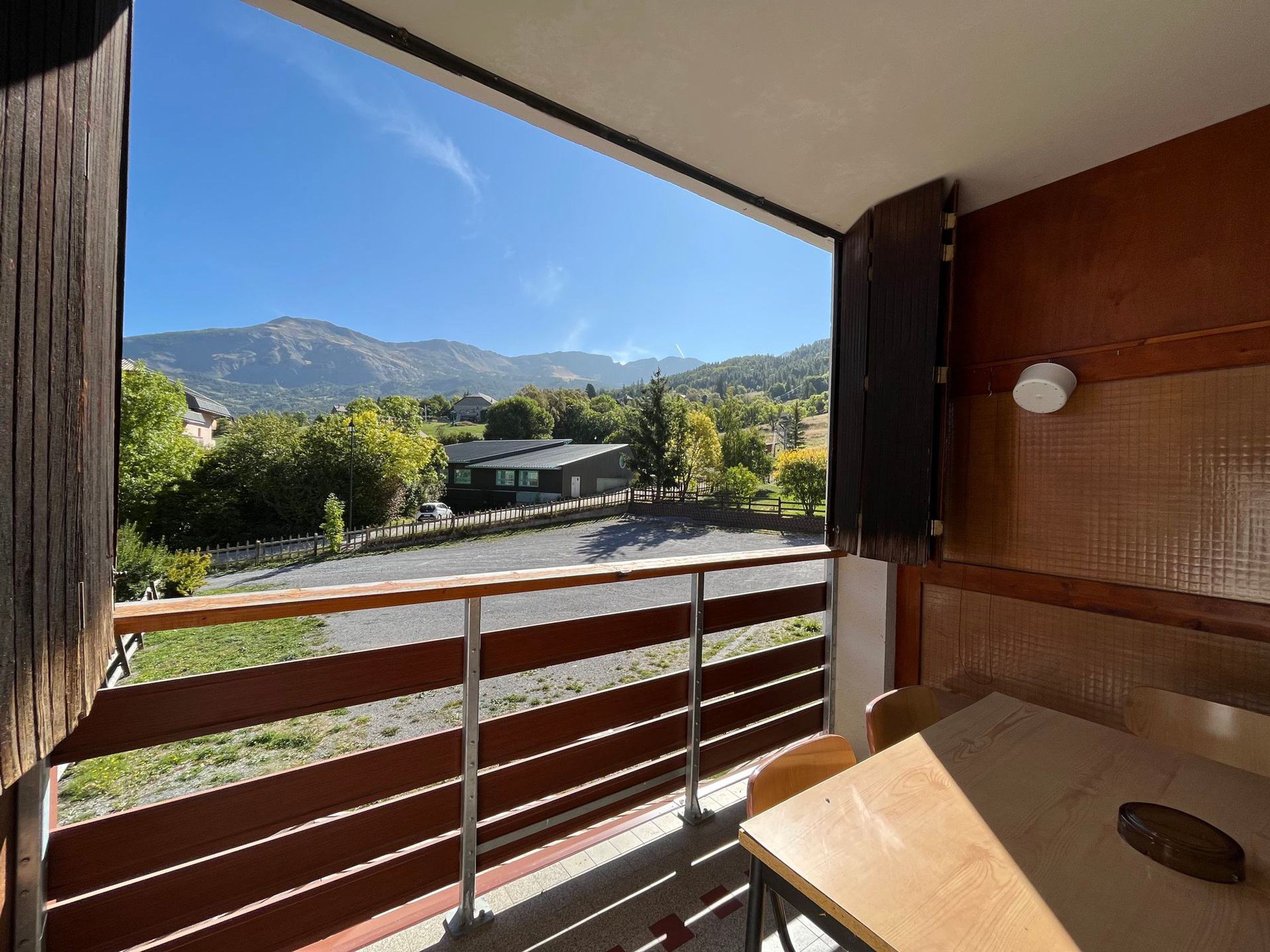 Una habitación con una mesa y banco de madera, una ventana con vistas a una montaña y un estacionamiento.