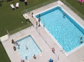 A rectangular swimming pool with a smaller adjacent pool, surrounded by a fenced area with lounge chairs and a grassy lawn. - Comfy Bungalow with Terrace - Sleeps 5, 2 Bedrooms (Zumaya)