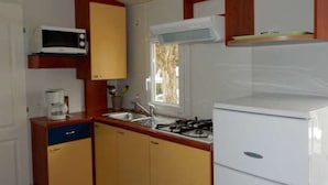 Una kitchenette compacta con microondas, estufa, pileta y alacenas de madera.