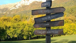 Un cartel de madera con flechas direccionales que señalan a varios destinos, como 'PIC DE CHARRANCE', 'COL BAYARD', 'TETE DE GUIZIERE', 'CEUSE' y 'LAC ET CHATEAU'.