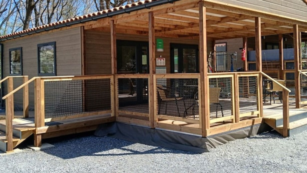 Una cabaña de madera con un porche cubierto, un área exterior cercada y un suelo de grava.