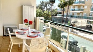 A balcony with a dining table set for four, white chairs, a white cabinet, and a view of a street with cars and buildings. - Vancouver Relax: Air-Conditioned Apartment with Pool, Parking, and 7-Min Walk to Cala Fon Beach (Salou)