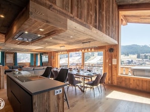 A modern kitchen with a large island, wooden walls, and a view of a snowy landscape. - Luxury Chalet in Les Gets with Jacuzzi, Wifi & Parking (Les Gets)