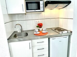 Cocina compacta con microondas, estufa, pileta y muebles de cocina blancos.