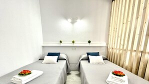 A room with two beds, each with a white towel and a flower, and a wooden slat wall. - Beachfront Loft with A/C and Pool, Near Port Aventura, Salou (Salou)