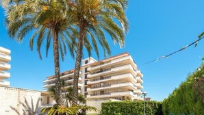 Un hotel de varios pisos con balcones, rodeado de palmeras y un césped cuidado.