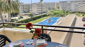 Un balcón con una mesa lista para comer, con vista a una piscina y un estacionamiento.
