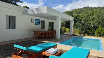 En moderne villa med pool, udendørs møbler og en overdækket terrasse.