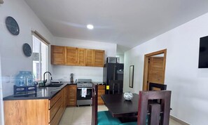 A compact kitchen with wooden cabinets, a stove, a refrigerator, and a dining table with chairs.