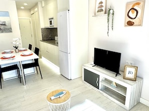 Una cuina moderna amb zona de menjador, televisió i una petita taula auxiliar.