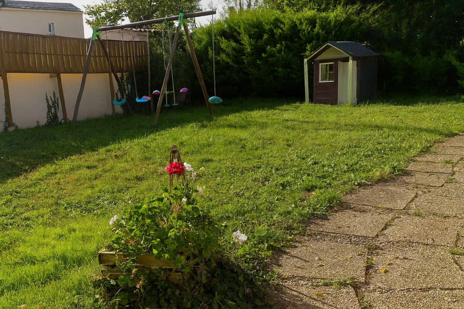 A backyard with a swing set, a small shed, and a garden with a wooden bench.
