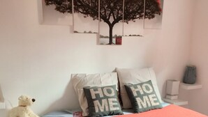 Ein Schlafzimmer mit einem Bett, Kissen, einem Teddybären, einer Wanddekoration mit Baumdesign und einem Regal mit einem Buch und einer Tasche.