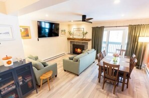 A living room with a fireplace, a television, a dining area, and a balcony with curtains.