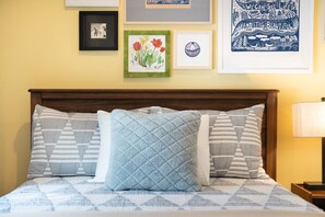 A bed with patterned bedding and pillows, a framed artwork above it, and a lamp on the side.
