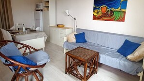 A modern living room with a sofa, two chairs, a small table, and a kitchen area with cabinets and a microwave. - Charming Apartment in Saint Pierre La Mer with Pool and Parking (Fleury-Saint-Pierre-la-Mer)