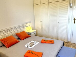 Un llit ben fet amb almoadins, una taula de nit amb una làmpada i un armari.