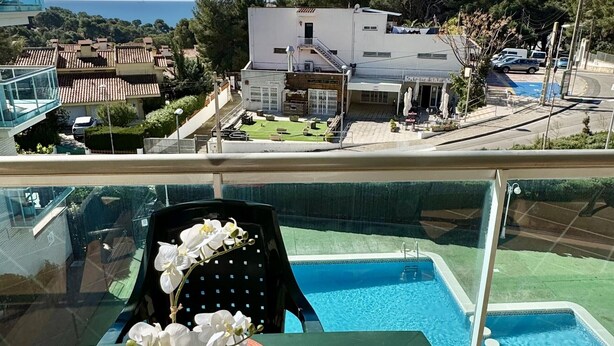 Un balcón con vista a una piscina, una mesa con un arreglo floral y una silla.