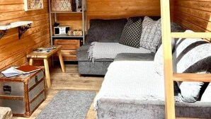 Interior acogedor de una cabaña con un sofá, una mesita, una estantería y una escalera.