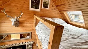 Una cabaña acogedora con interior de madera, una cama con ropa de cama floral, una chimenea de piedra y cuadros en las paredes.