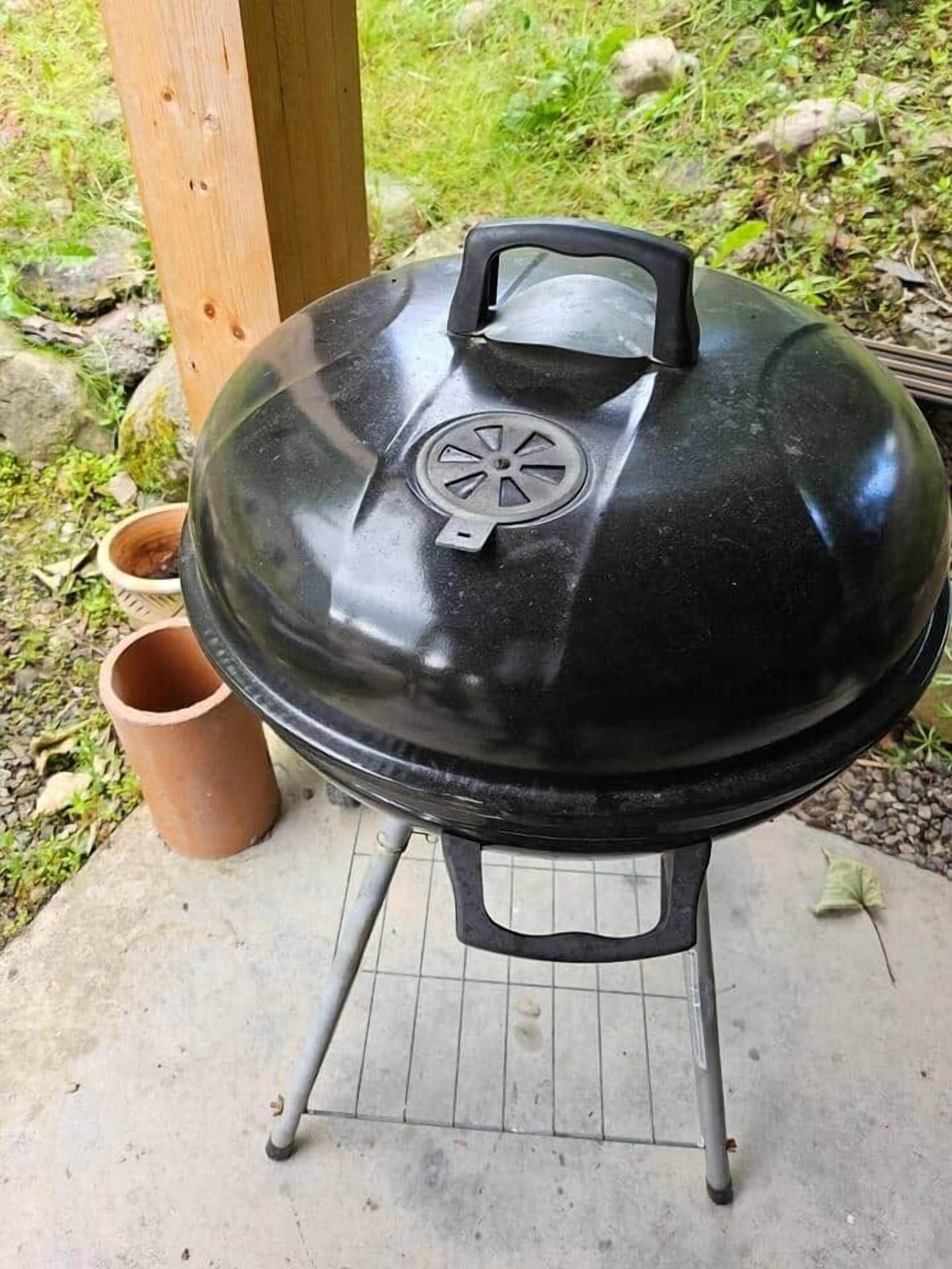 A black barbecue grill with a lid, a metal stand, and a terracotta pot nearby.